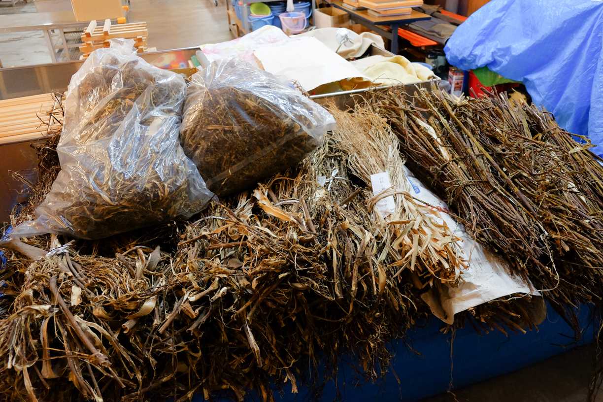 Pile de fibres végétales séchées et de tiges liées sur une table, tons bruns et beiges, ambiance rustique